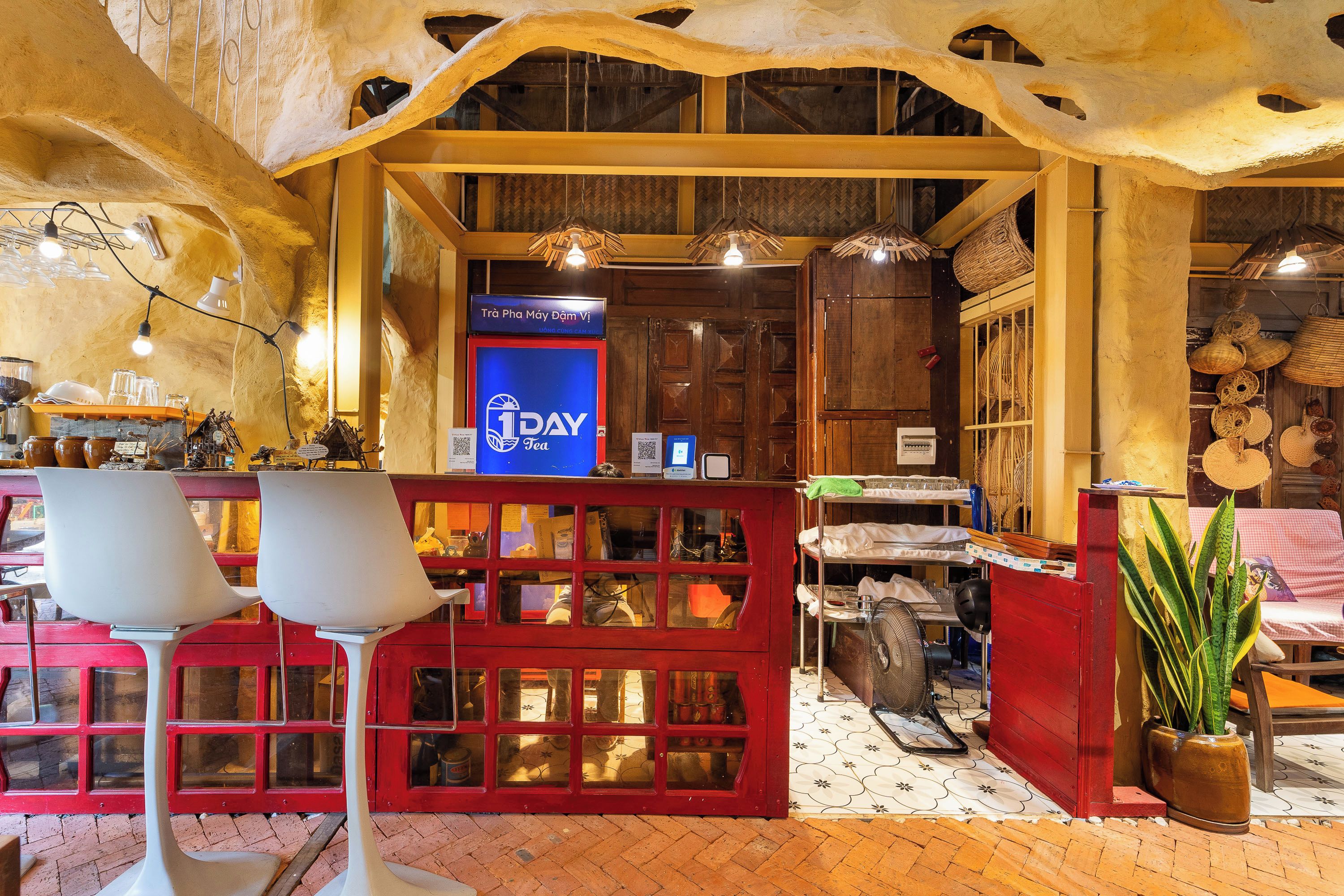 A restaurant interior with a red booth seating area, a blue sign with '1DAY Tea' text, and various kitchen utensils visible through the booth windows.