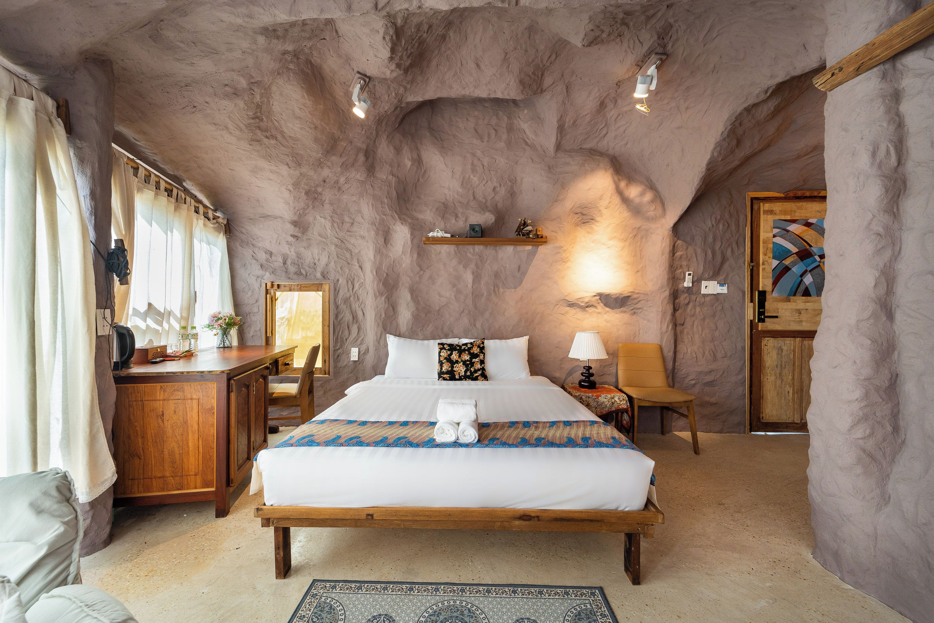 Ein Schlafzimmer mit rustikalem Stein-Gewölbe, einem Holzbett, einem Schreibtisch mit Stuhl und einer kleinen Ablage mit Dekorationen.