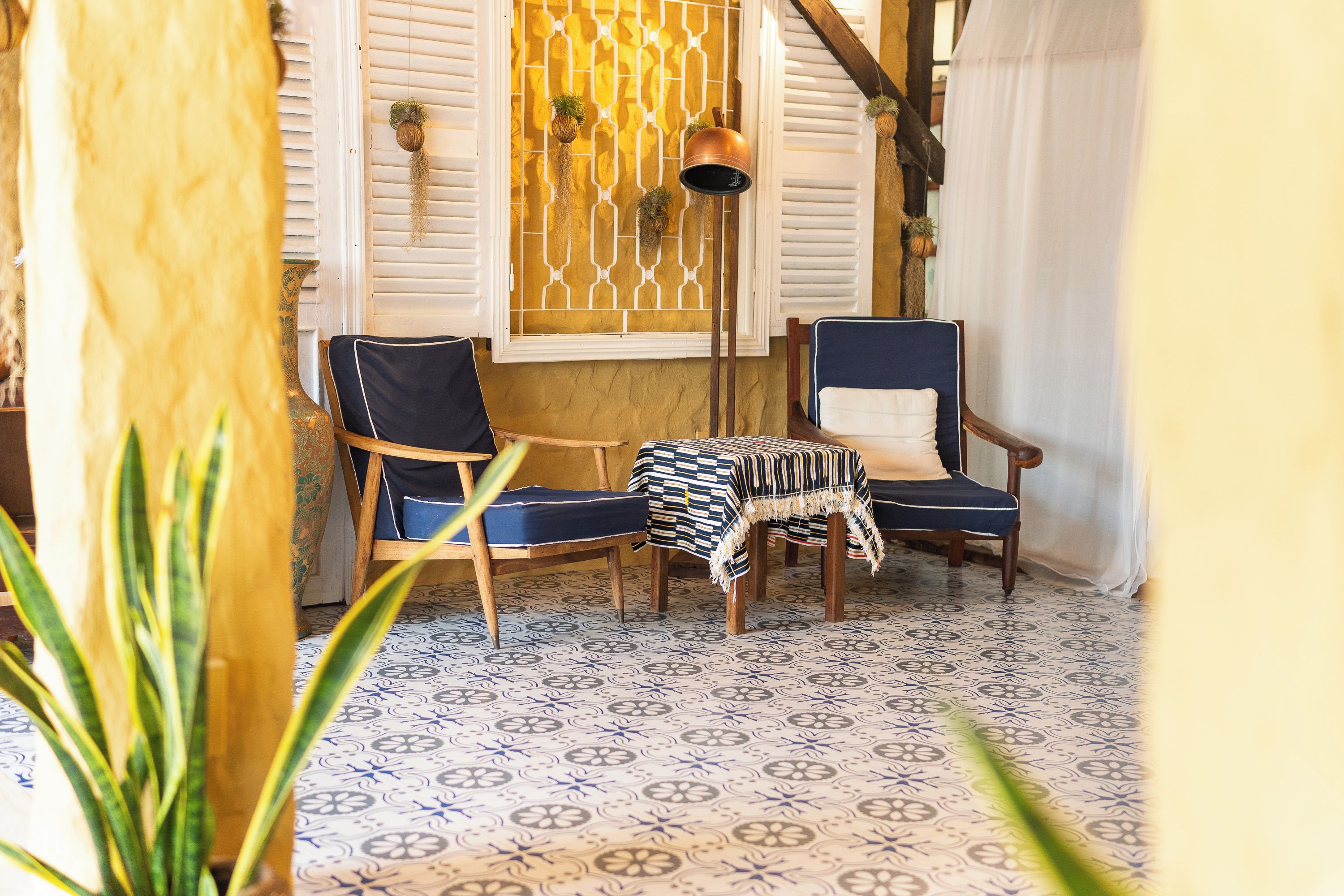 A room with two chairs, a small table, patterned floor tiles, and a decorative window with shutters.