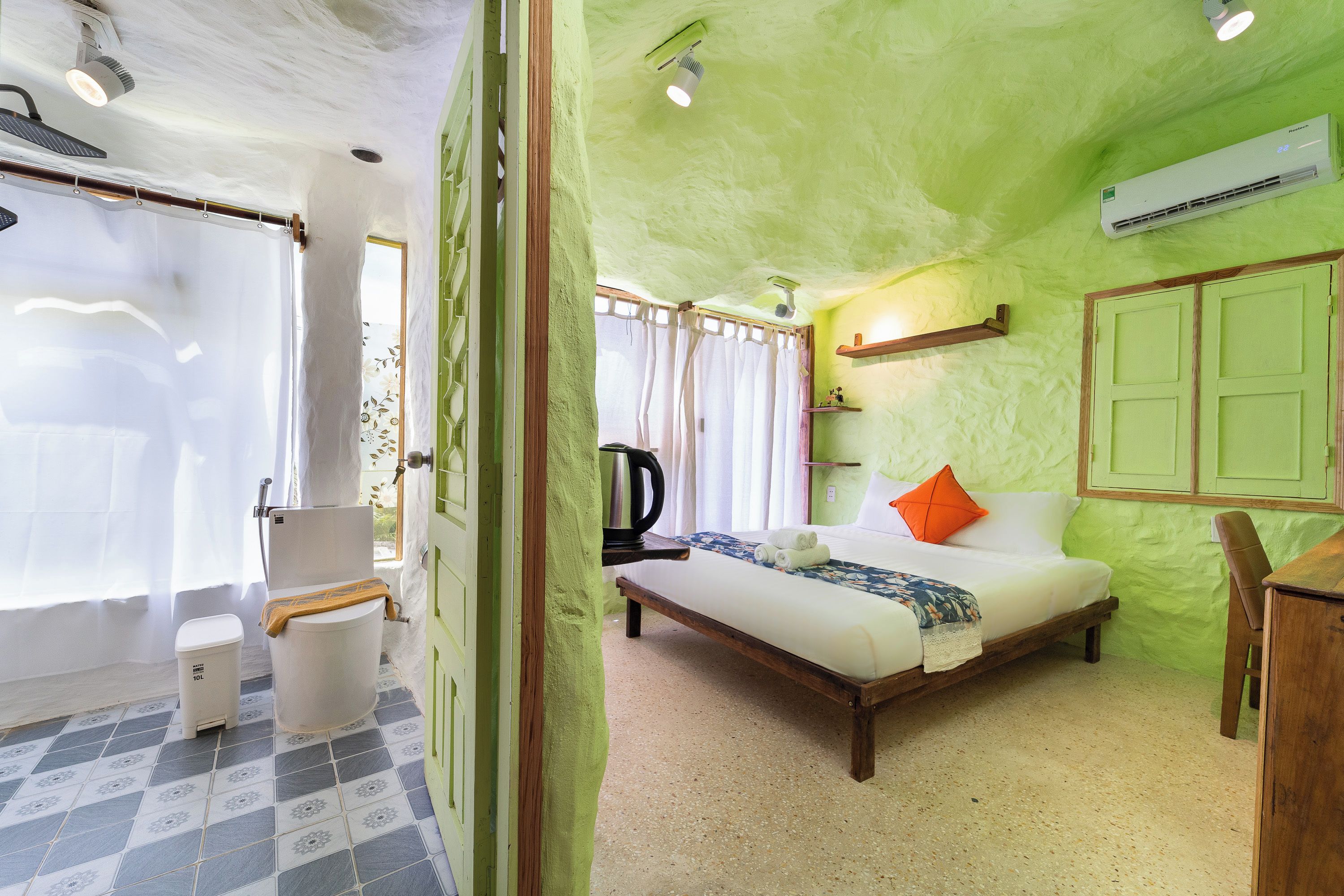 A room with a bed, a bedside table, a window with curtains, a radiator, and a wall-mounted shelf.