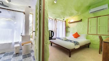 A room with a bed, a bedside table, a window with curtains, a radiator, and a wall-mounted shelf.