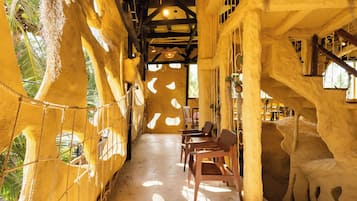 Una stanza con soffitto alto, travi in legno e lampadario a sospensione. Sono presenti tavoli e sedie disposti per la ristorazione.