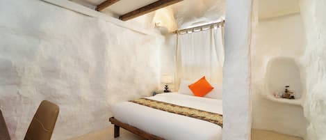 A bedroom with a bed, a chair, a bedside table, and a wall-mounted air conditioning unit.