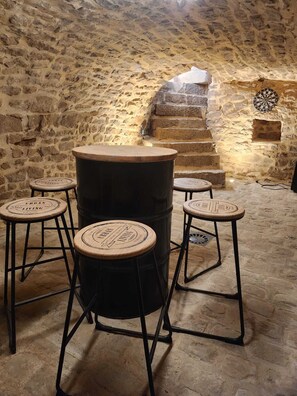 Un rincón de bar rústico con pared de piedra, un barril de madera y taburetes con la marca 'Urban Living'.