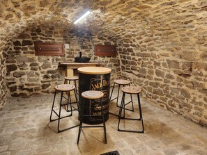 Ein Raum mit Steinwänden, einer Holztresore, Barhocker und einem großen Fass mit der Aufschrift 'Jack Daniel's'.