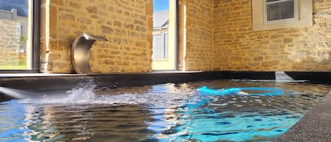 An indoor swimming pool with stone walls, large windows, and ceiling fans.