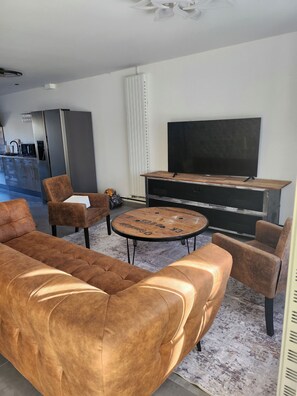 Una sala de estar con un sofá, sillones, una mesa de centro, un televisor de pantalla plana y un mueble empotrado para entretenimiento.