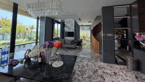 A modern interior with a marble floor, a chandelier, a sofa, and a view of greenery outside. - Luxury Villa Near My Khe Beach (Đà Nẵng)