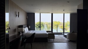 A modern hotel room with a large bed, a desk, a chair, and a view of the city through large windows. - Luxury Villa Near My Khe Beach (Đà Nẵng)