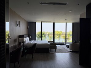 Habitación de hotel moderna con una cama grande, un escritorio, una silla y vistas de la ciudad a través de amplias ventanas.