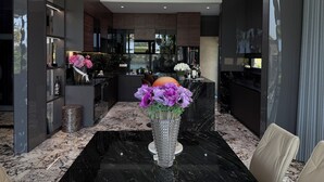 A modern kitchen with dark cabinetry, a marble countertop, and a central island. - Luxury Villa Near My Khe Beach (Đà Nẵng)