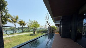 A modern building with a long, narrow pool, a wooden deck, and a view of a lake and trees. - Luxury Villa Near My Khe Beach (Đà Nẵng)