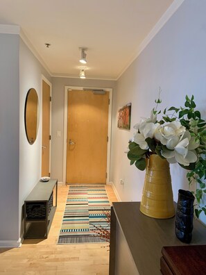 A hallway with a wooden door, a patterned rug, a vase with white flowers, and a small bench. - 2 bed 2 bath NOPA Fully Equipped Quiet Beauty in San Francisco with a Peloton (San Francisco)