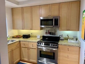 A kitchen with wooden cabinets, a microwave, a toaster, a stove, and a knife rack. - 2 bed 2 bath NOPA Fully Equipped Quiet Beauty in San Francisco with a Peloton (San Francisco)