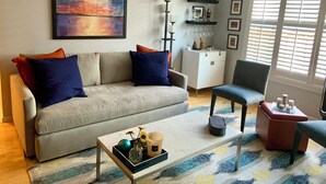A living room with a sofa, armchair, coffee table, and a painting on the wall. - 2 bed 2 bath NOPA Fully Equipped Quiet Beauty in San Francisco with a Peloton (San Francisco)