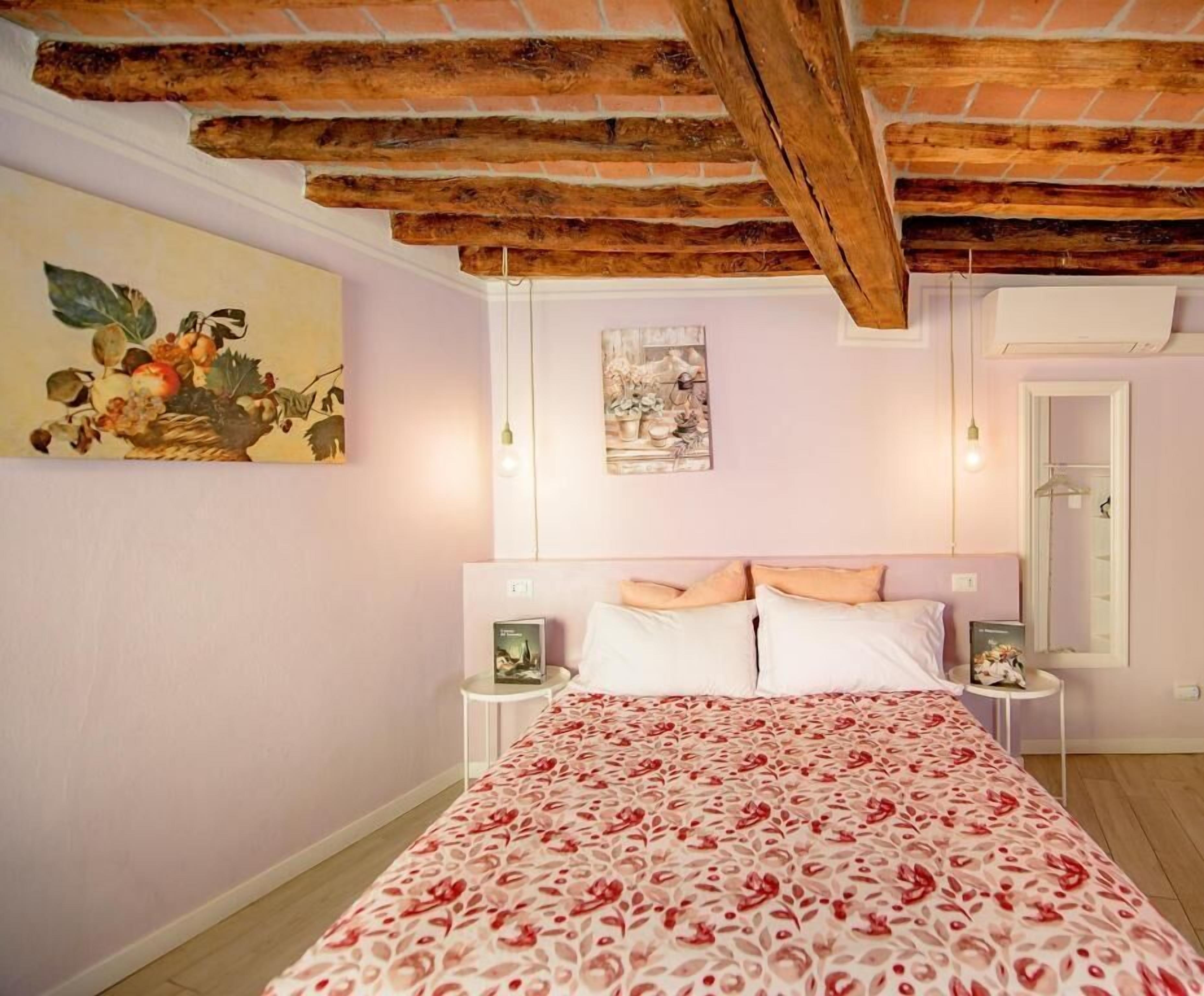 A bedroom with a bed, two bedside tables, a hanging light, a wall painting, and a door.