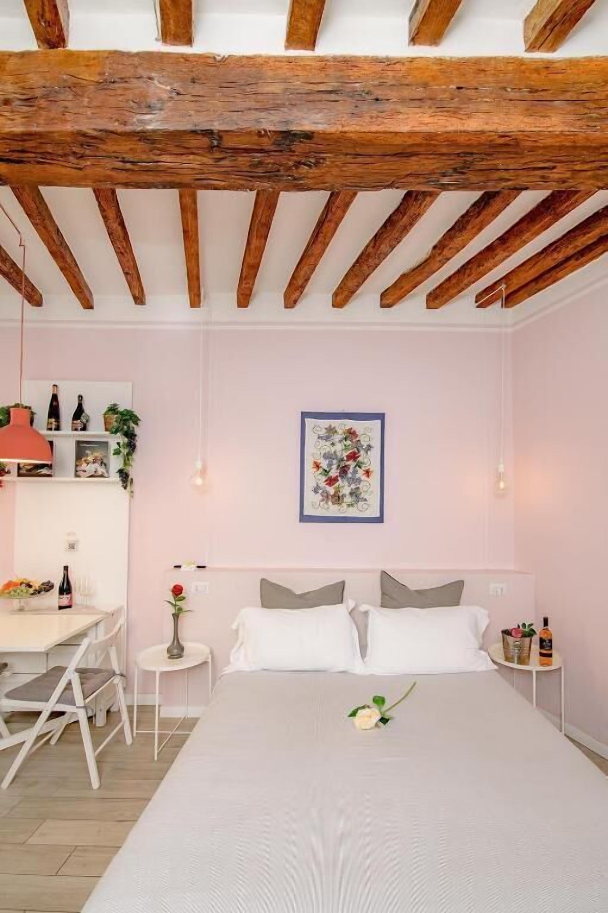 A bedroom with a wooden ceiling, a bed with white bedding, a bedside table, a small round table, and a wall-mounted picture.