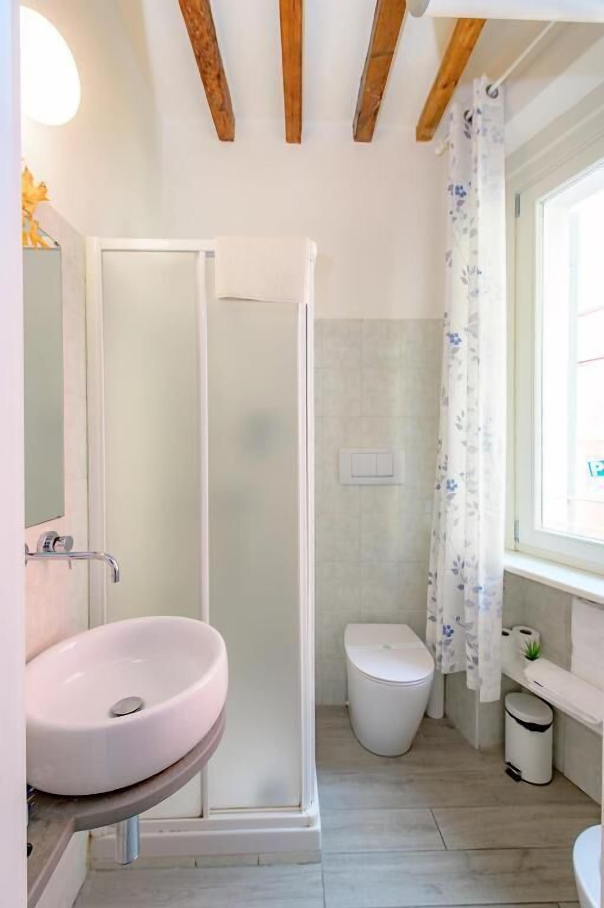 A bathroom with a shower, toilet, sink, and a window with a curtain.