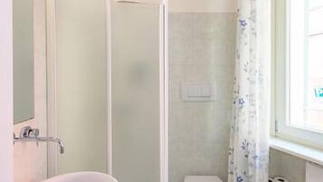 A bathroom with a shower, toilet, sink, and a window with a curtain.