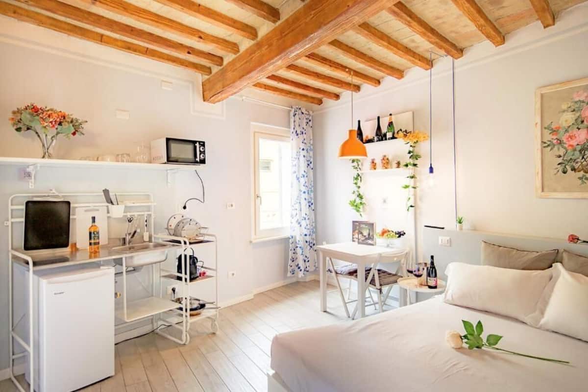 Un dormitorio con cama, escritorio, microondas, refrigerador pequeño y ventana con cortinas.