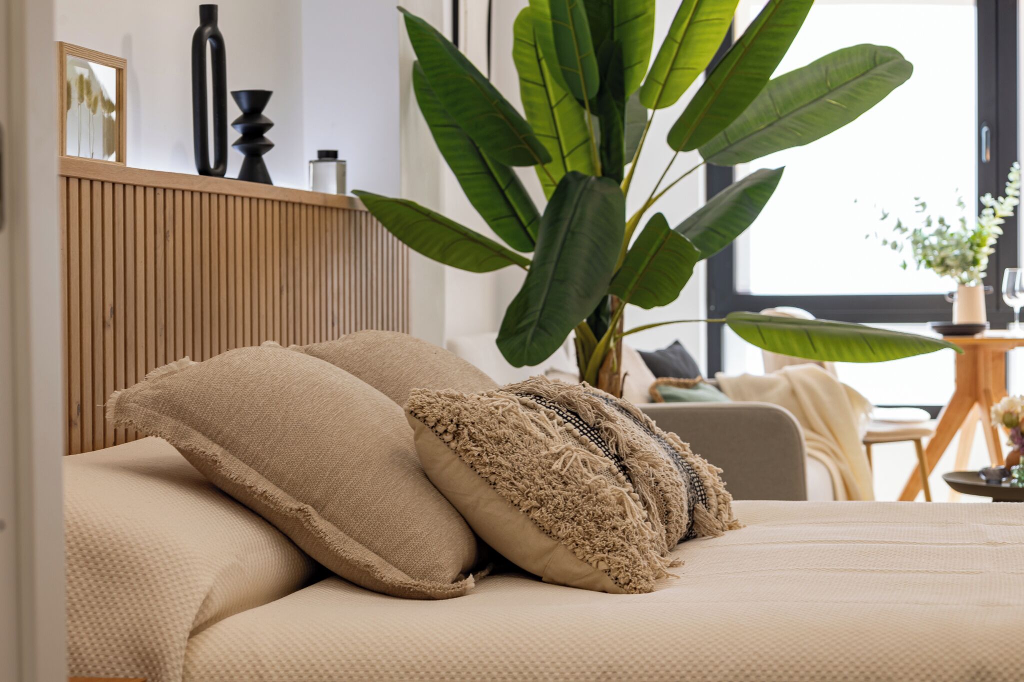 Un dormitorio con cama, almohadas, una planta grande y vistas al exterior.