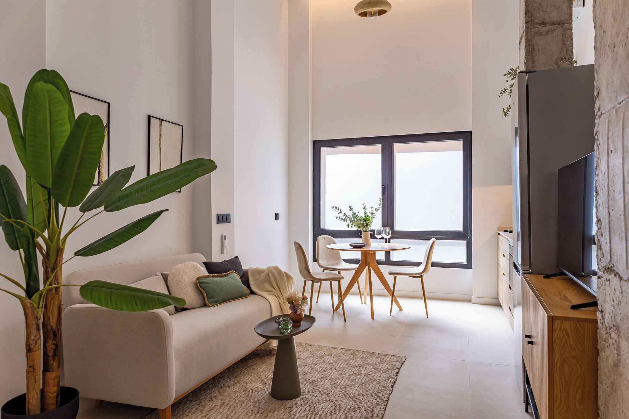 A modern living room with a sofa, coffee table, dining table, chairs, and a TV.