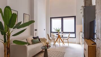 A modern living room with a sofa, coffee table, dining table, chairs, and a TV.