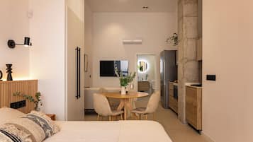 A modern hotel room with a bed, bedside table, lamp, and a view into the dining area.