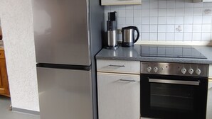 A compact kitchen with a stainless steel refrigerator, a coffee maker, a stove, and white cabinets.