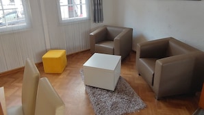 A living room with a sofa, two armchairs, a yellow ottoman, a white coffee table, and a painting on the wall.