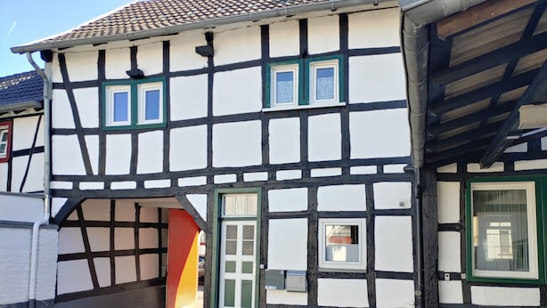 A traditional half-timbered house with a visible entrance, a small window, and a mailbox.