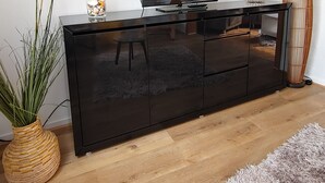 A modern living room with a black entertainment center, a flat-screen TV, a woven floor lamp, and a potted plant.