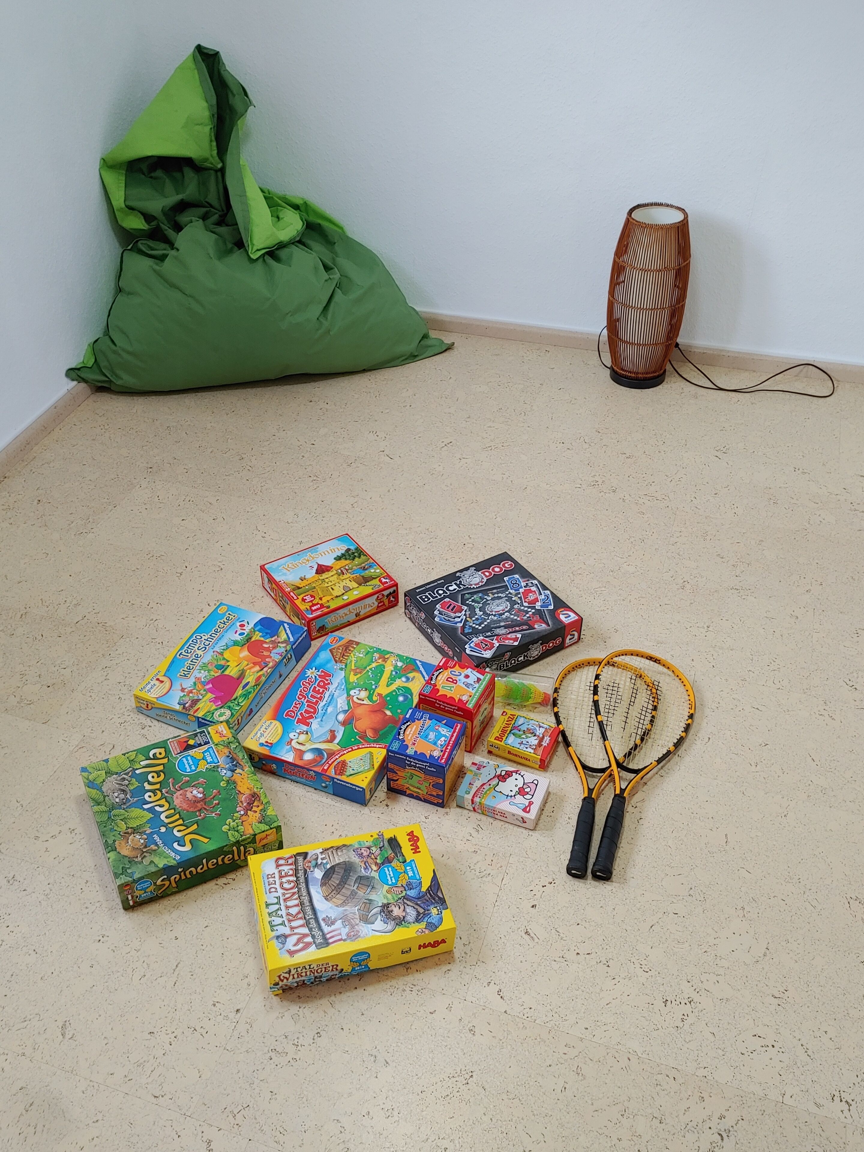 A room with a green bean bag chair, a woven floor lamp, and various children's board games and toys on the floor.