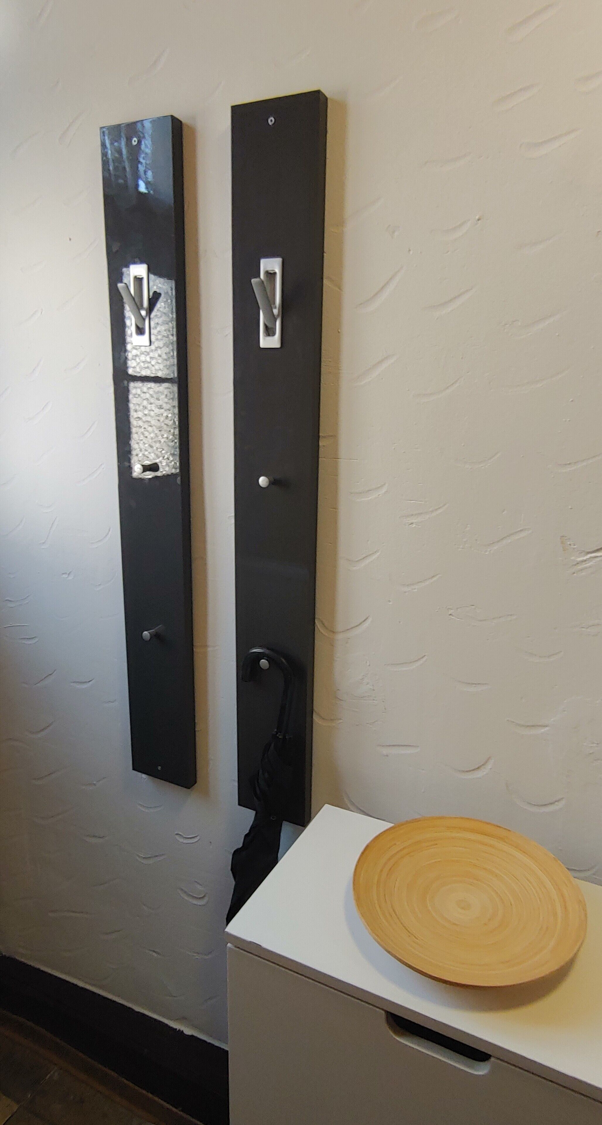 A wall-mounted metal panel with a textured surface and a white cabinet with a wooden tray.