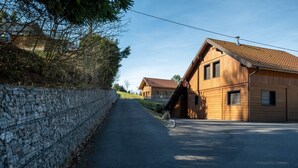 Camí pavimentat que condueix a un edifici de fusta amb teulada inclinada, una paret de pedra a un costat i un cel serè.