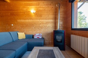 Interior de una cabaña de madera con sofá, chimenea y ventana.