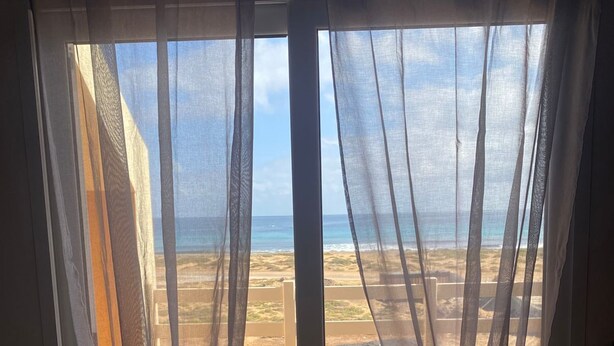 A room with a view of a beach through sheer curtains. - La Vedetta Bella Vista Ocean View (Santa Maria)