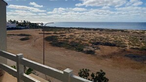 A coastal view with a dirt path leading to the beach, a clear sky, and a building with a balcony. - La Vedetta Bella Vista Ocean View (Santa Maria)