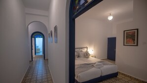 Una habitación de hotel con piso estampado, una cama con almohadas y una colcha, una mesita de noche con lámpara, y un cuadro en la pared.