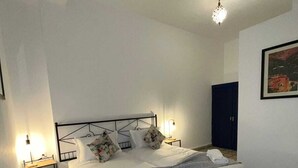 Un dormitorio ordenado con cama, dos mesitas de noche, lámpara colgante, alfombra estampada y un cuadro en la pared.