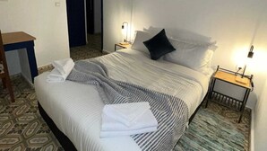 Una cama bien hecha con almohadas y una toalla doblada, una mesita de noche con una lámpara y una alfombra estampada.