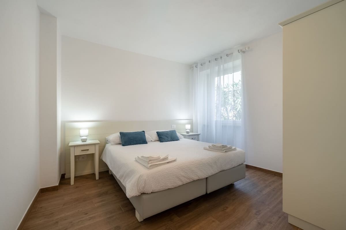 A minimalist bedroom with a bed, two bedside tables, and a window with sheer curtains.