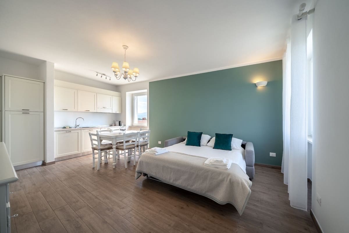 A bedroom with a bed, a desk, and a kitchenette.