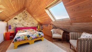 Un dormitorio con techo inclinado, una cama con colcha colorida, una silla y una pequeña mesa con lámpara.