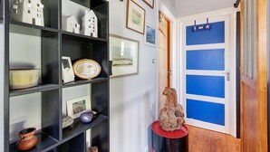 Un pasillo con estanterías negras que exhiben varios objetos, una puerta con marco azul y suelo de madera.