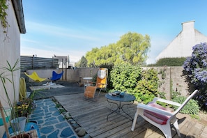 Une terrasse en bois avec des meubles d’extérieur, un chemin en pierre et un jardin agrémenté de diverses plantes.