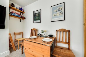 A dining area with a wooden table set for two, two chairs, a small cabinet, and two framed botanical prints on the wall. - Florence of Oxford (Oxford)