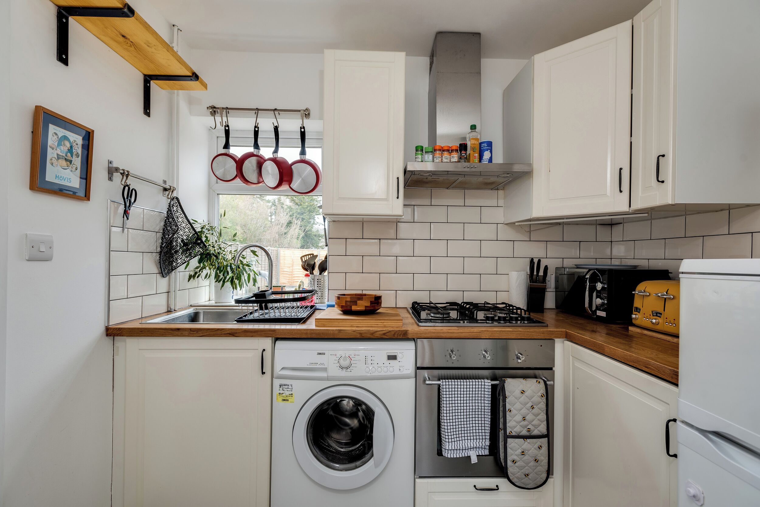 Une cuisine de taille réduite, équipée d’un lave-linge, d’une cuisinière et d’une petite fenêtre.