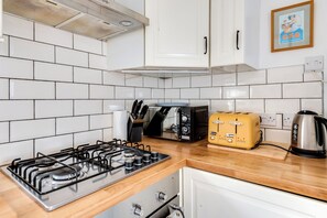 Una cocina con paredes de azulejos blancos, una estufa a gas, un tostador y un hervidor.