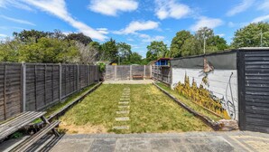 Ein Garten mit gepflasterter Terrasse, Holzzaun und Wandgemälde.